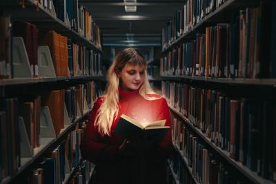 Woman standing in library stacks with a lit-up book.