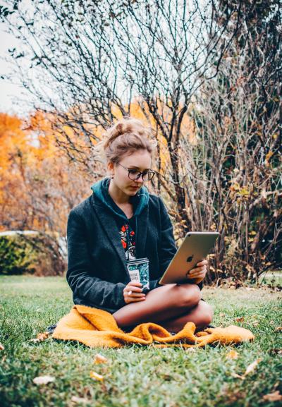 woman sitting in grass reading from a tablet 